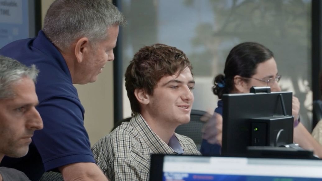 An instructor leaning in to help a student at a trading desk